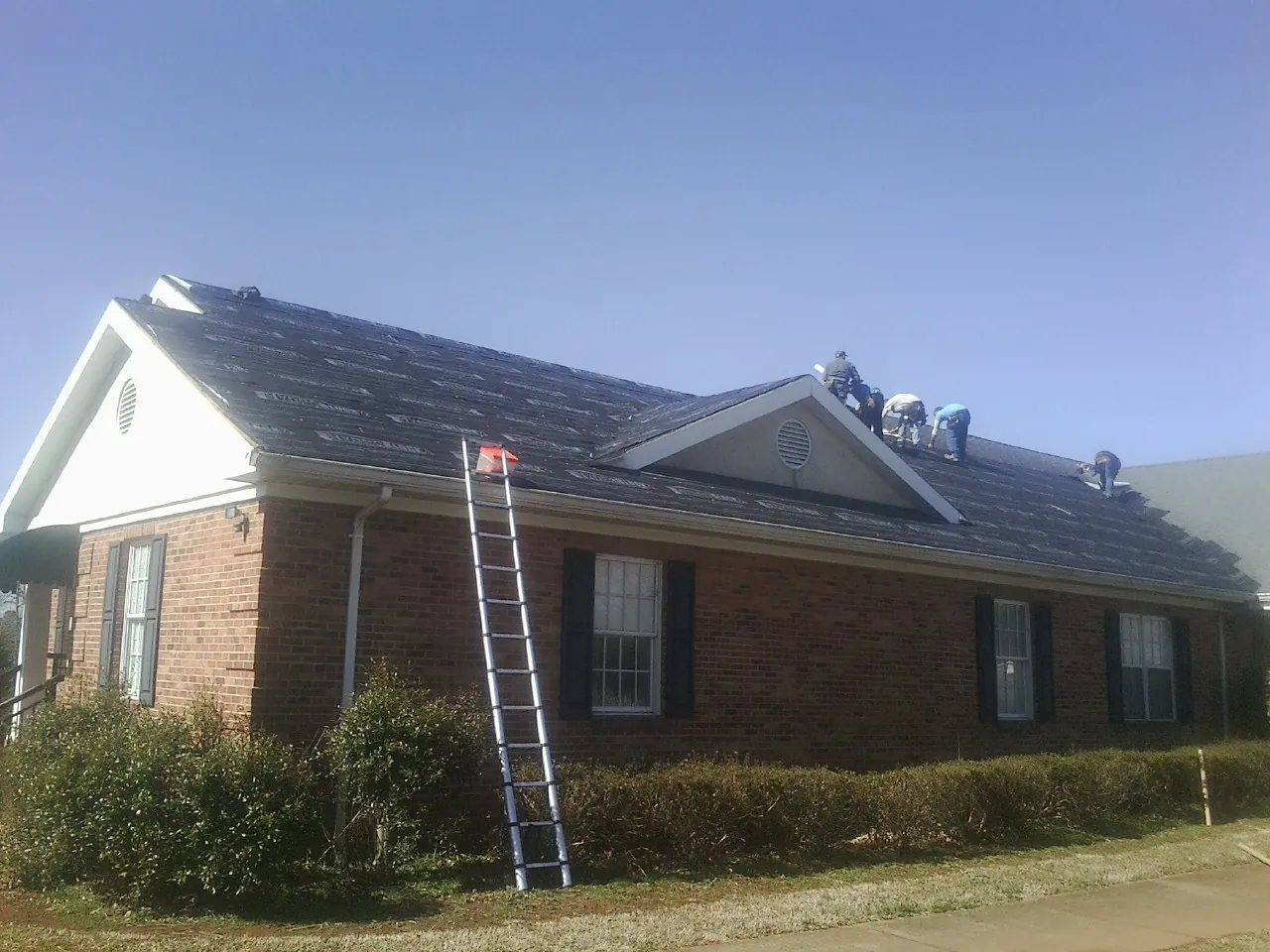 Crew tearing shingles off a brick ranch roof with a ladder set — Emergency Roof Repair work by our crew in Belvidere