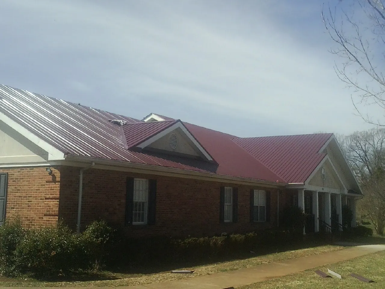 Red metal roof with gabled entries on a long brick building, from a Hail Damage Roof Repair job in Belvidere