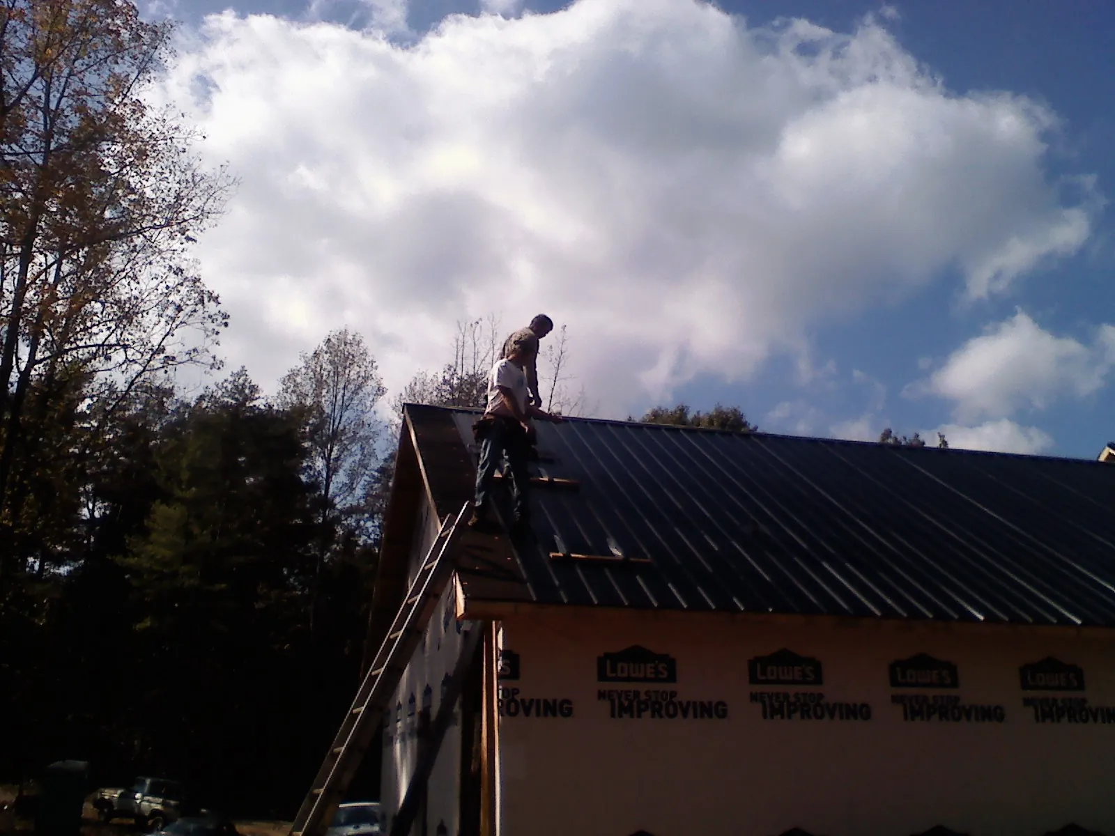 Roofer fastening dark metal panels high against a cloudy sky, from a Roof Inspection job in Belvidere
