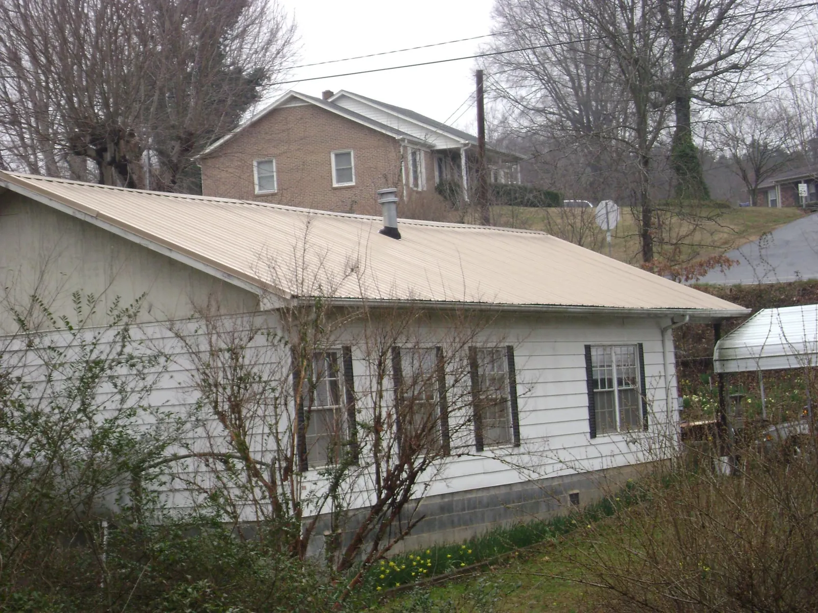 Tan metal roof on a white sided house set into a hillside — Commercial Roofing by Roofing Brothers in Belvidere